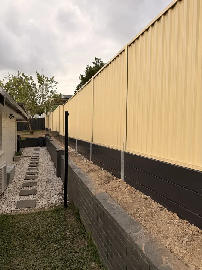 Two-tone Colorbond fence in cream with a dark base panel above a brick retaining wall