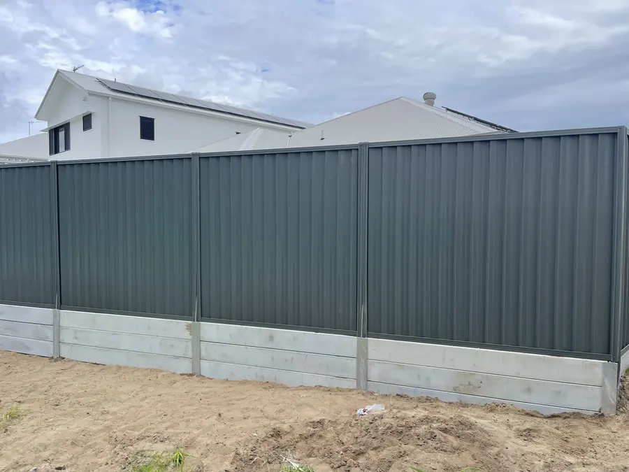 Green Colorbond fence on a grey concrete sleeper plinth at a new build