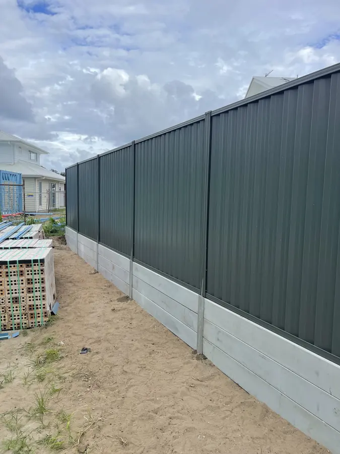 Concrete sleeper plinth stepping down a slope beneath a Colorbond boundary fence