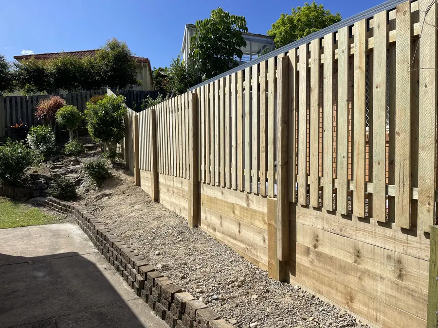 Spaced treated pine paling fence on a sleeper retaining wall beside a driveway